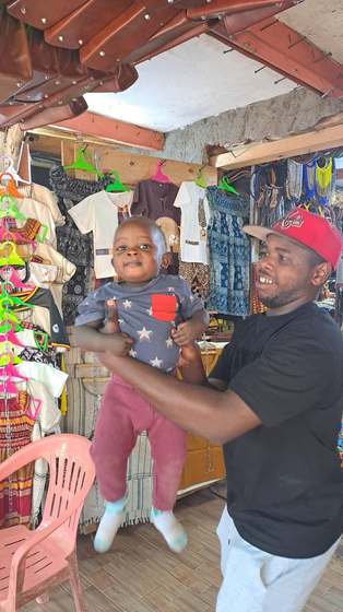 A vendor shares a smile with a little one at a boutique stall in a Kampala market.